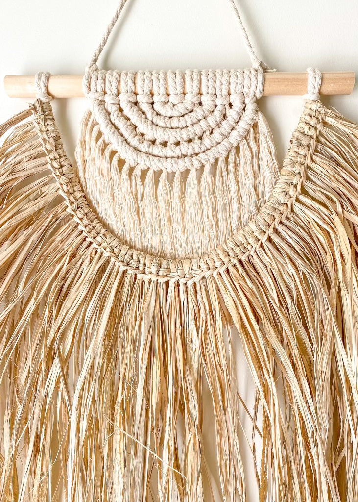 Close up iew of the front of macrame and raffia wall hanging hanged on a wall