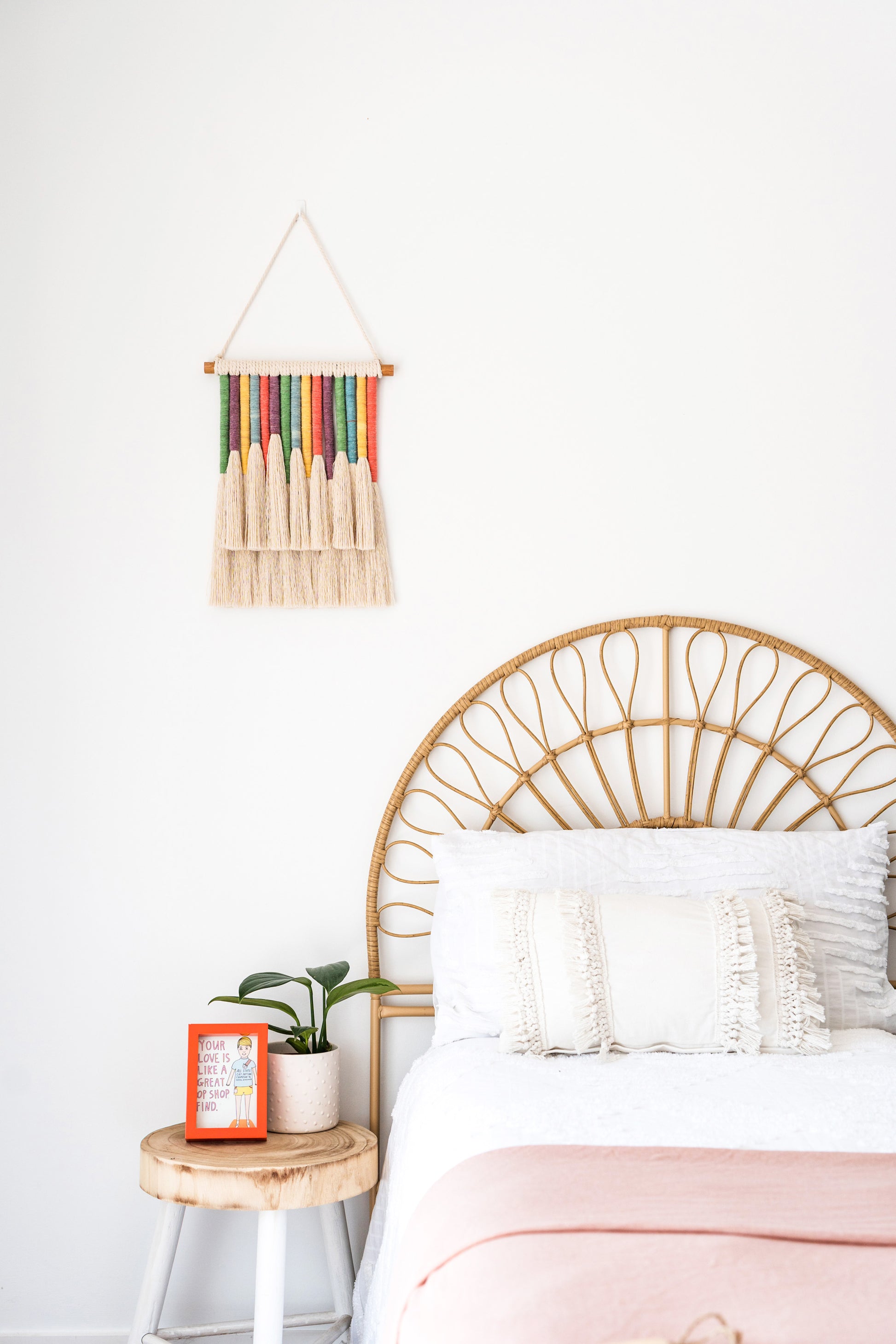 Rainbow tassels wall hanging hanged on a wall above a rattan bed in a kids bedroom