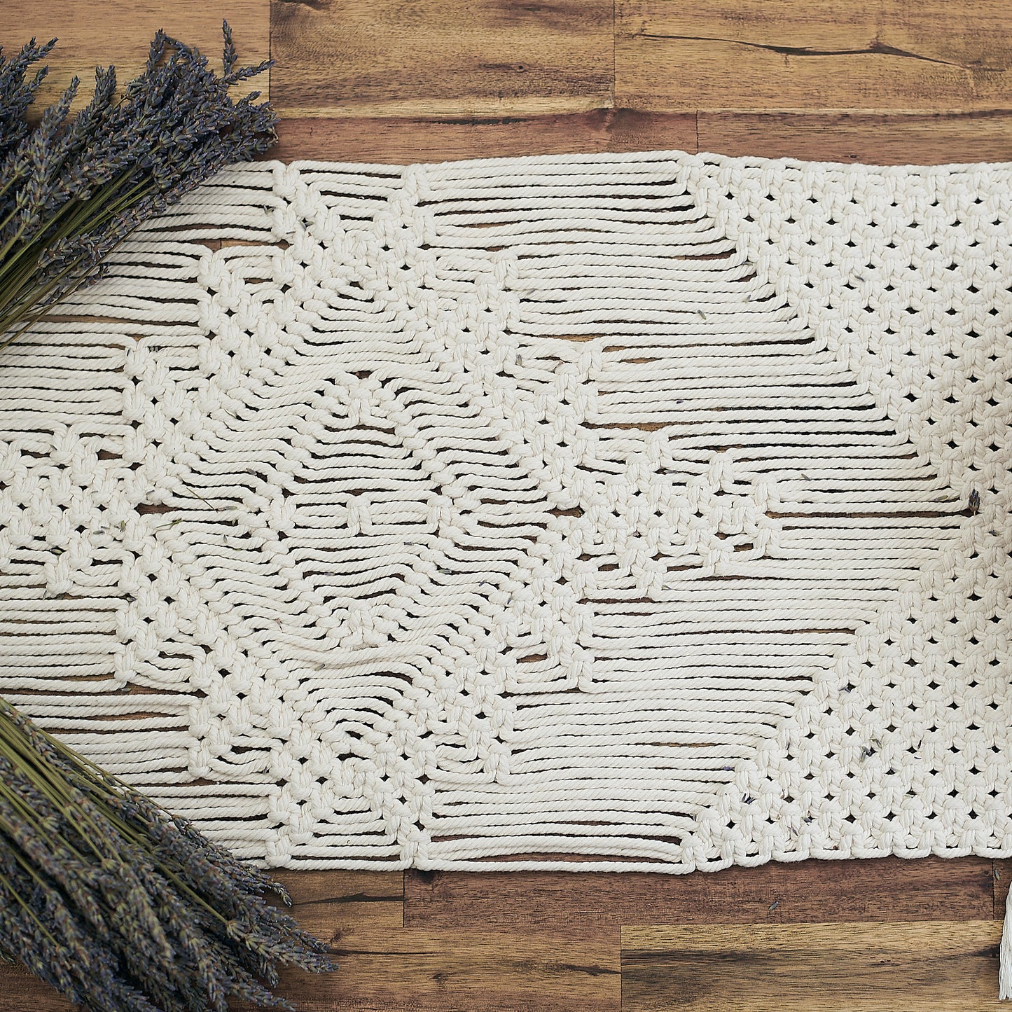 Close up view of natural white macrame table runner on a wooden table styled with rustic dried Lavender
