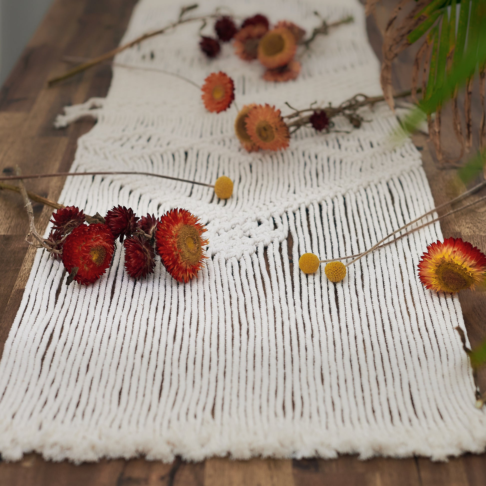 Natural white macrame table runner on a wooden table styled with rustic dried flowers