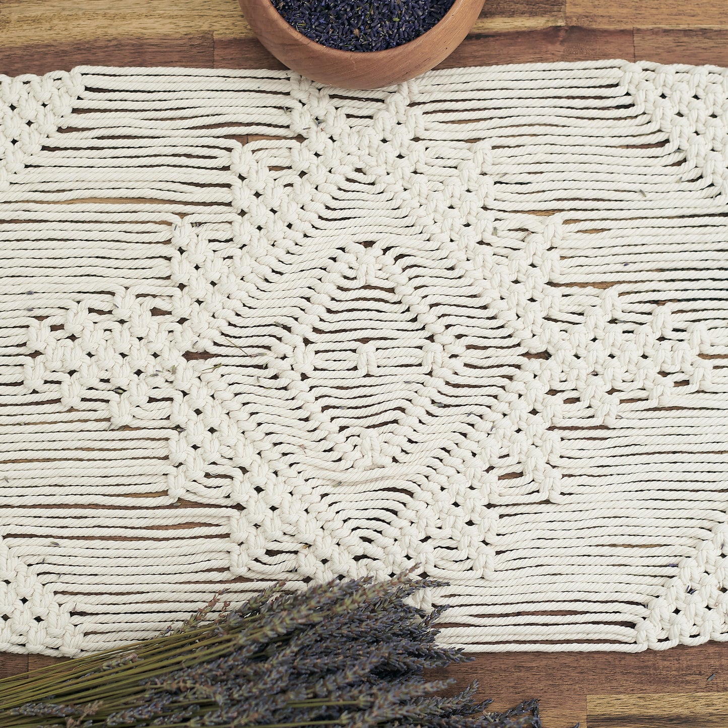 Natural white macrame table runner on a wooden table styled with rustic dried Lavender and pottery