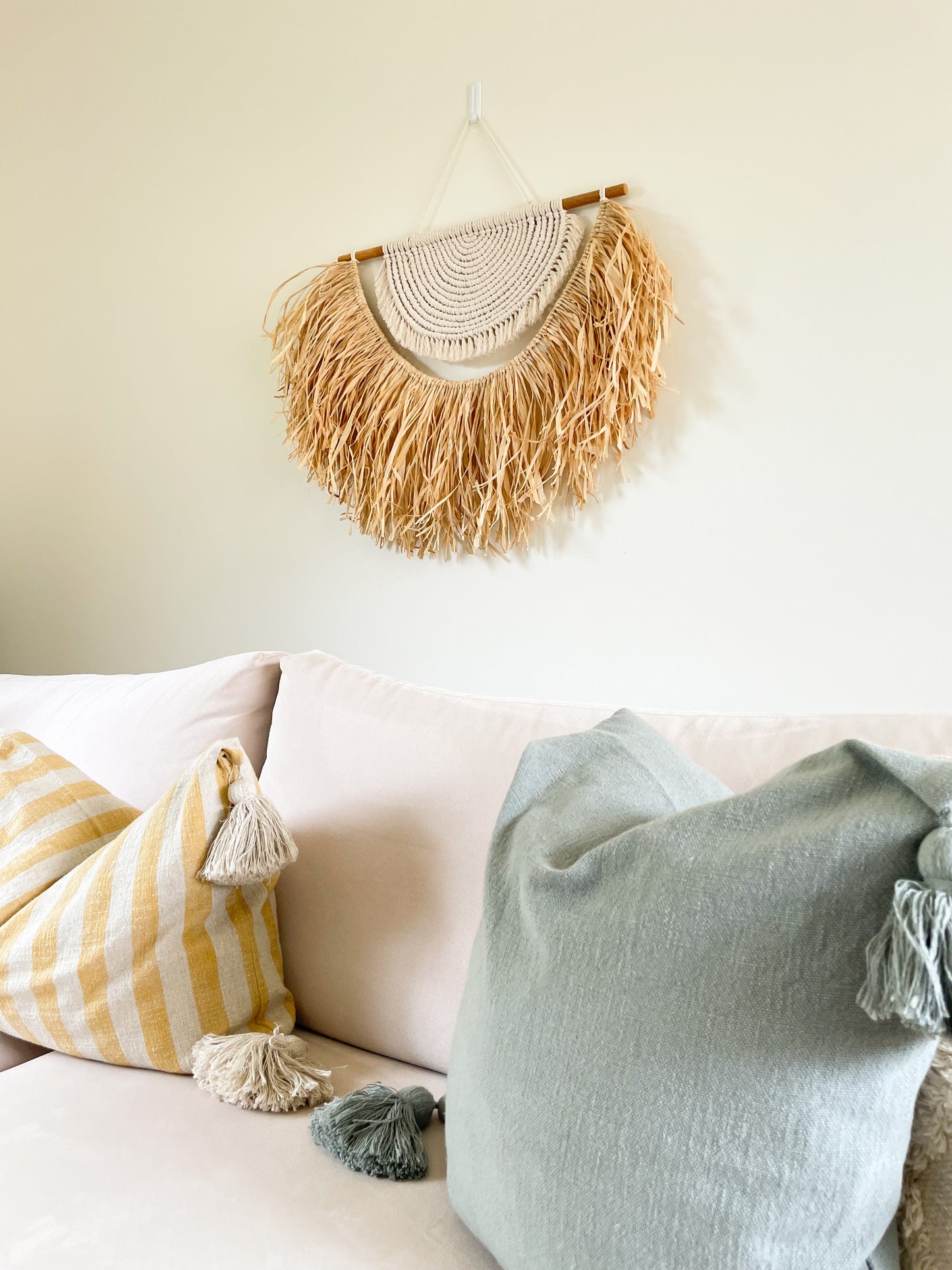 Large macrame and raffia wall hanging hanged on a wall above a large sofa styled with coastal style cushions