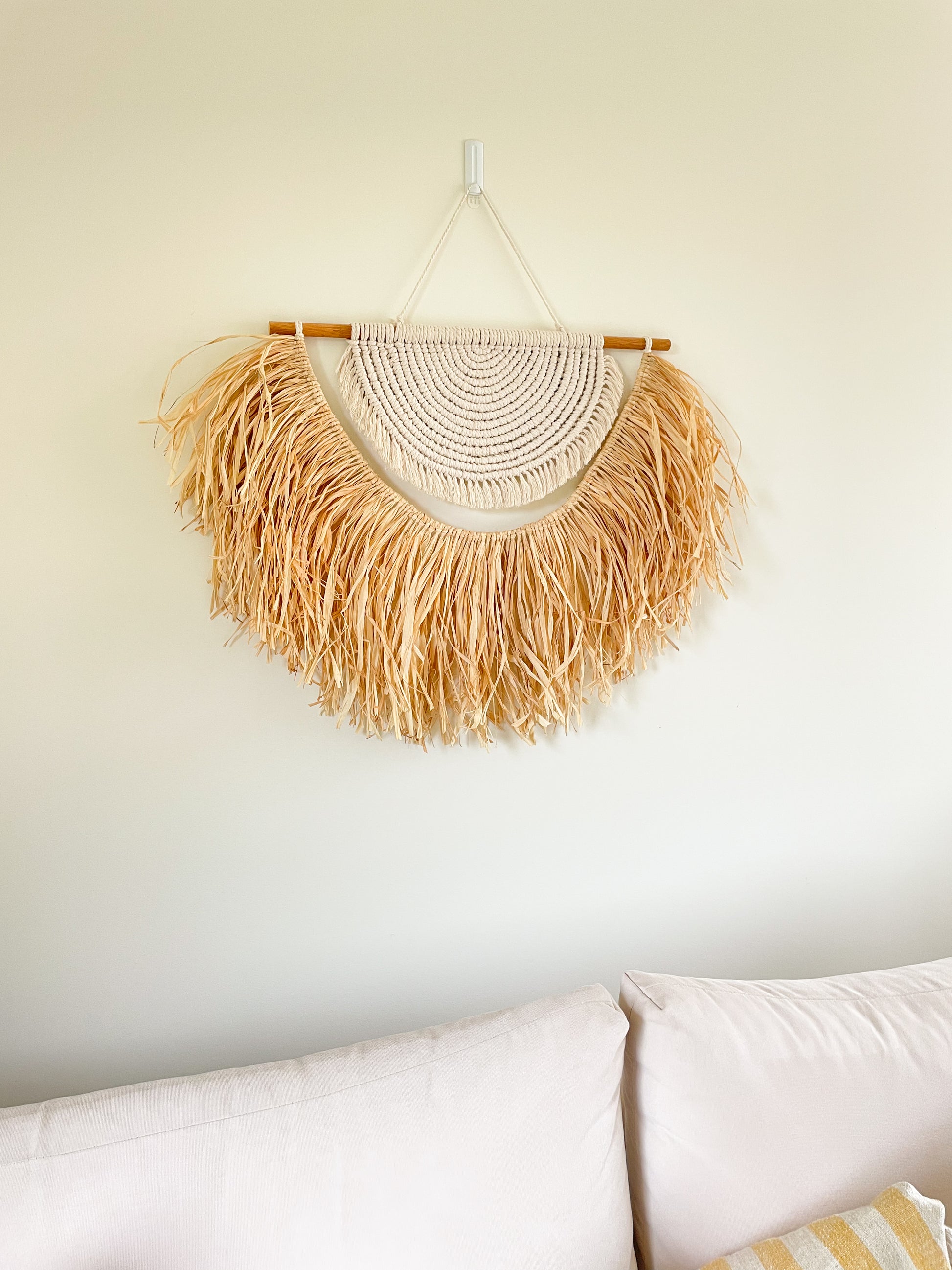 Large macrame and raffia wall hanging hanged on a wall above a large sofa