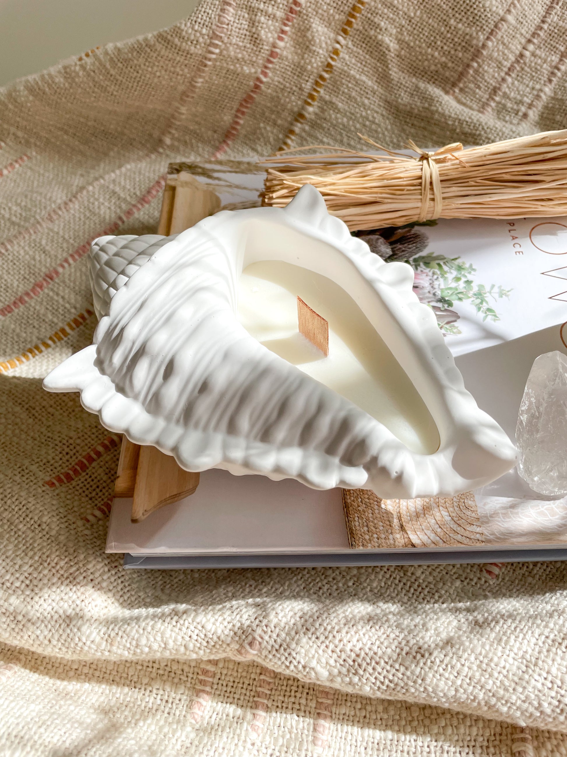 Seashell soywax candle styled on a coffee table book with crystals and rattan ornaments