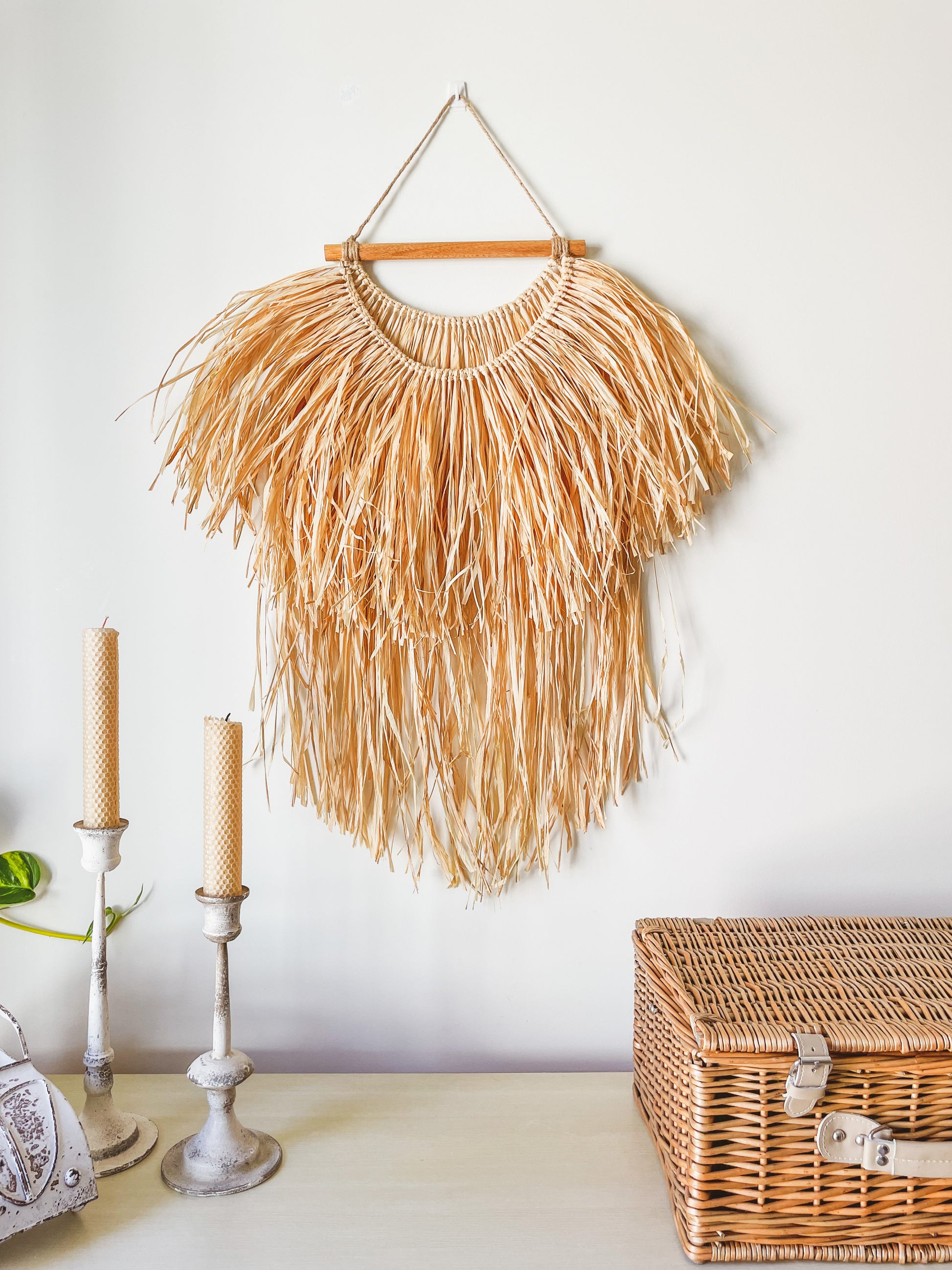 Large raffia wall hanging hanged on a wall above a sideboard styled with a rattan picknic basket and candles