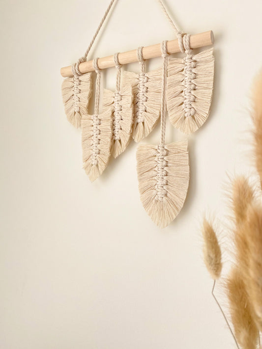 Macrame feather wall hanging hanged on a wall decorated with dried wild flowers