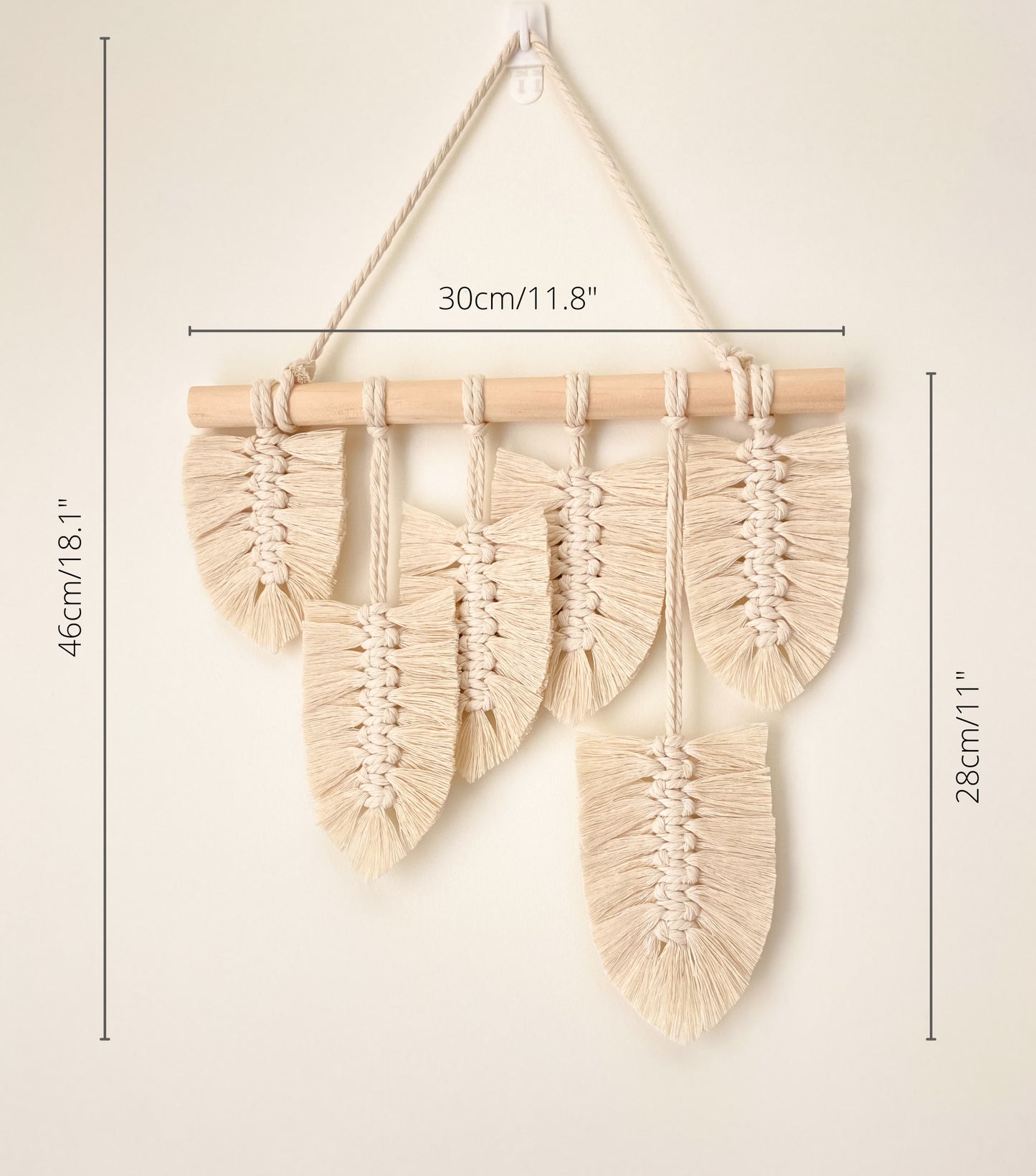 Natural white macrame feather wall hanging hanged on a wall. Dimensions are marked. 