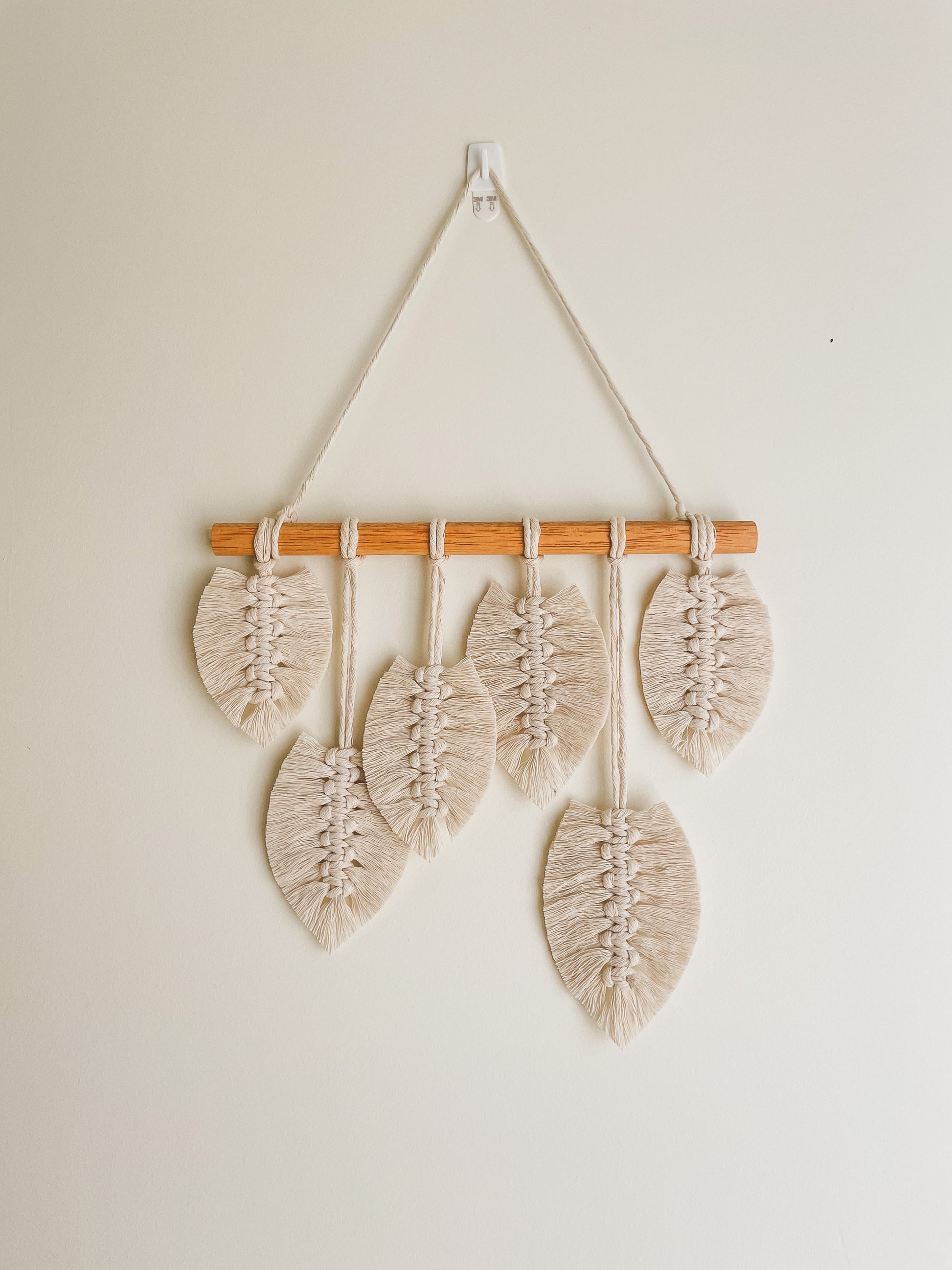 Close up view of Sunshine macrame leaves hanging hanged on a wall. Ceramic vase placed next to it with a dried branch from a tree
