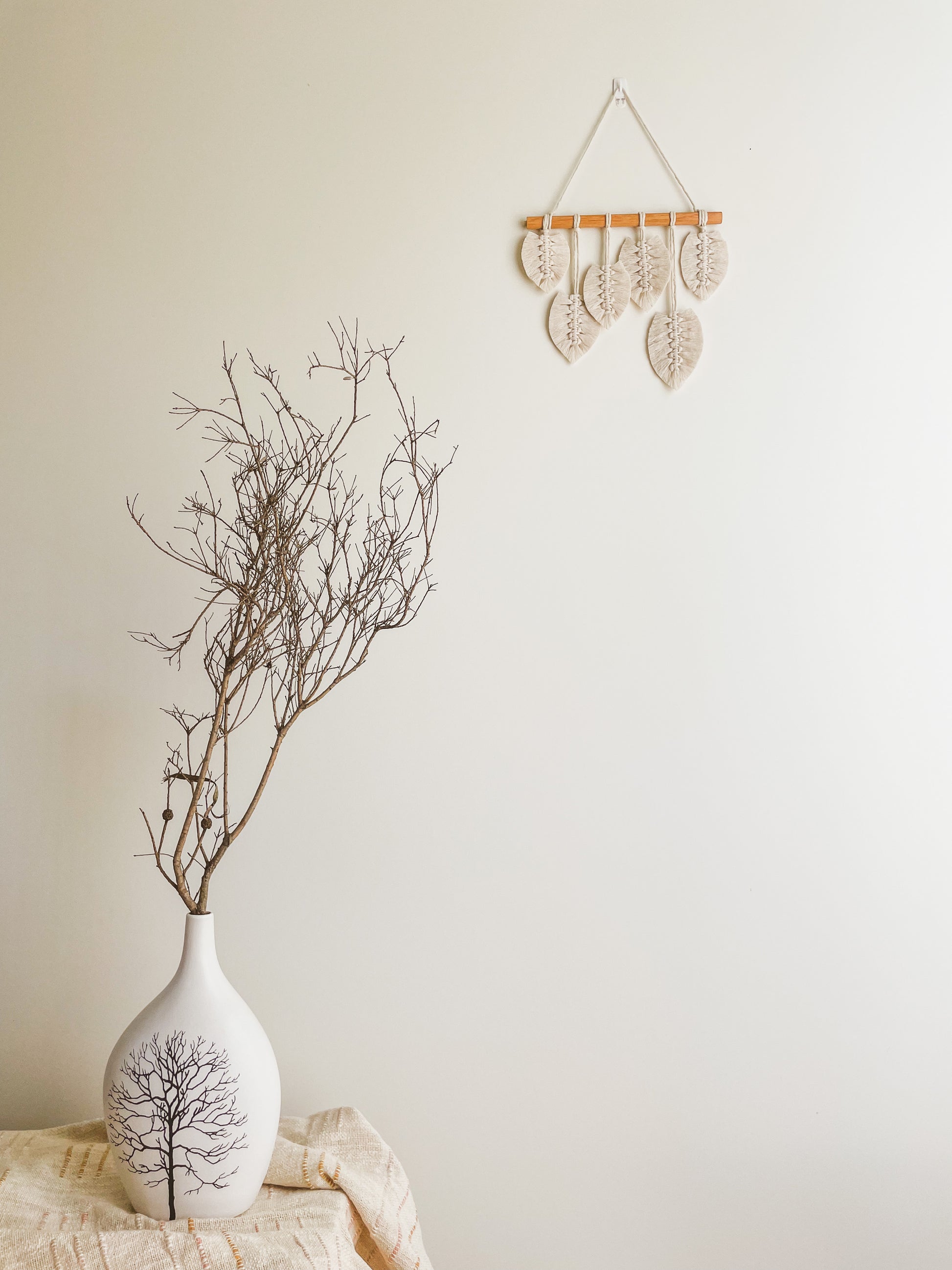 Sunshine macrame leaves hanging hanged on a wall. Ceramic vase placed next to it with a dried branch from a tree
