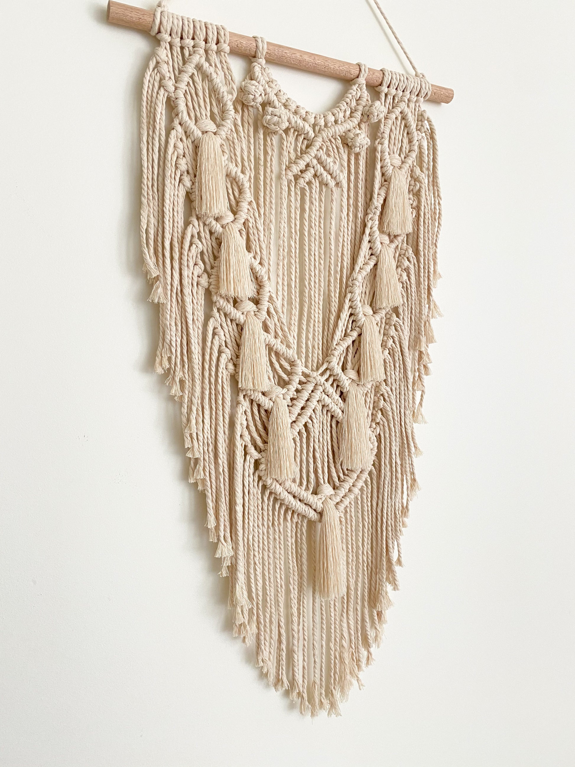 Side view of a natural white macrame wall hanging hanged on a white wall 
