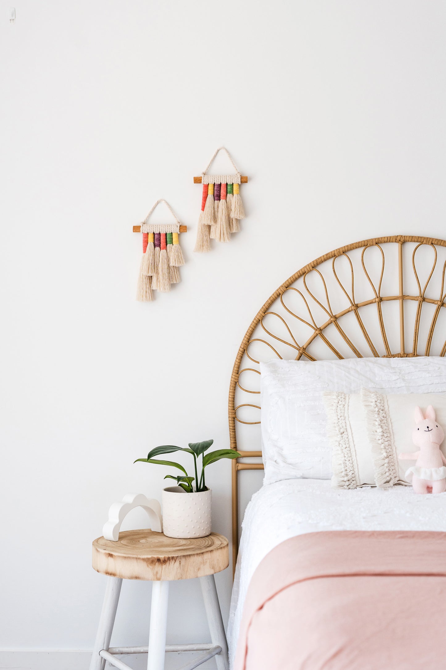 Two small rainbow macrame wall hangings hanged on the wall of a coastal themed kids bedroom.