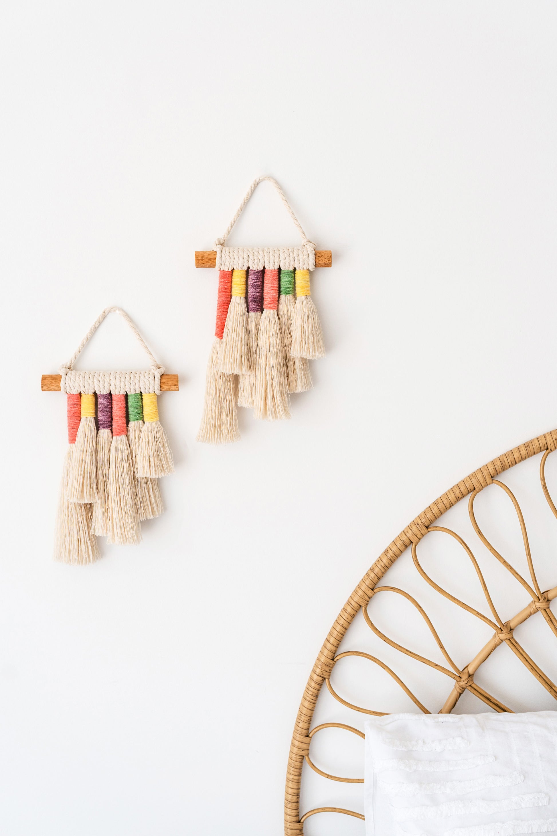 Close up photo of two mini rainbow macrame wall hangings hanged above the bed of a coastal themed kids bedroom
