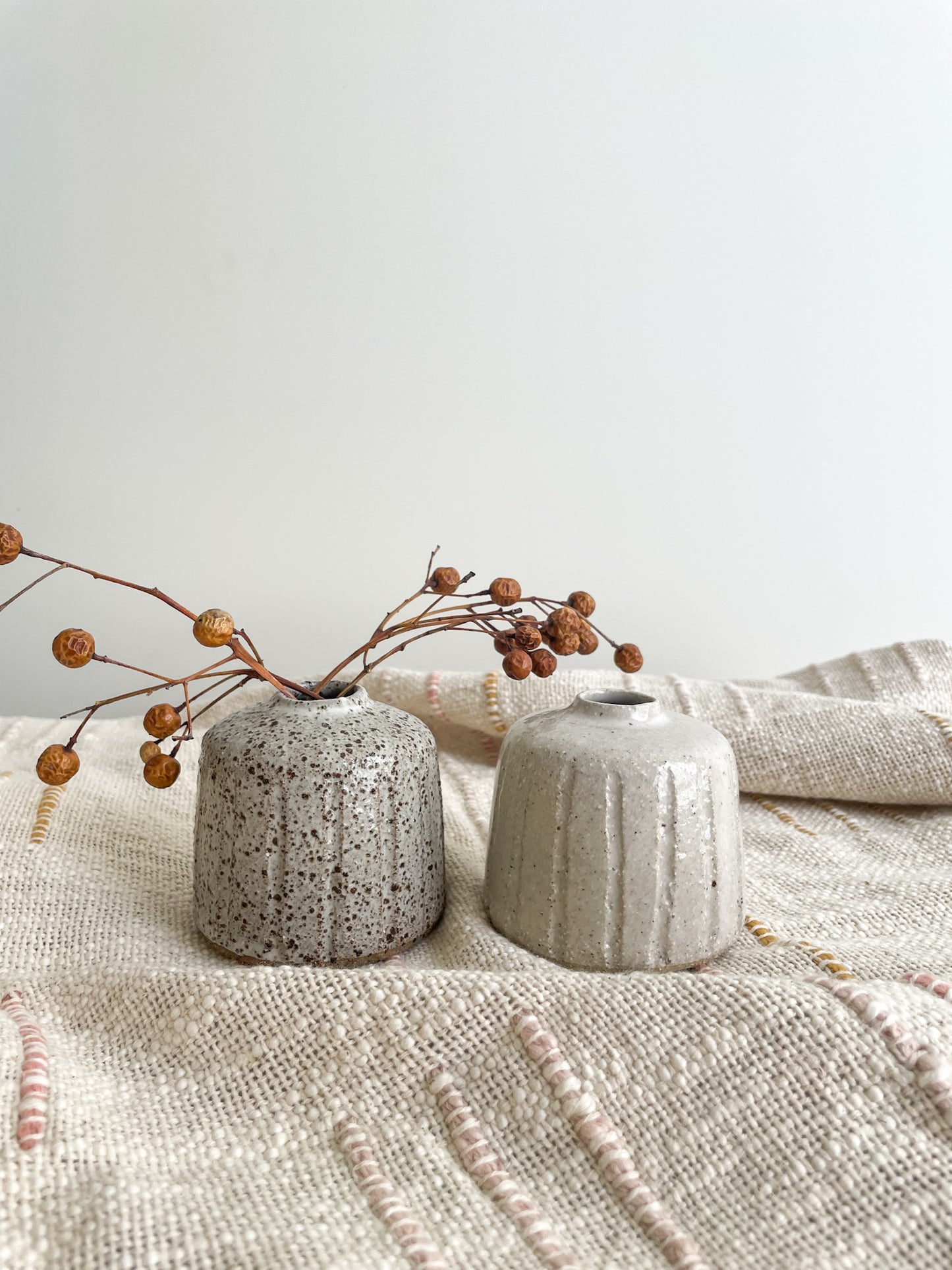 White samll ceramic vases displayed on a piece of fabric and styled with dried flowers