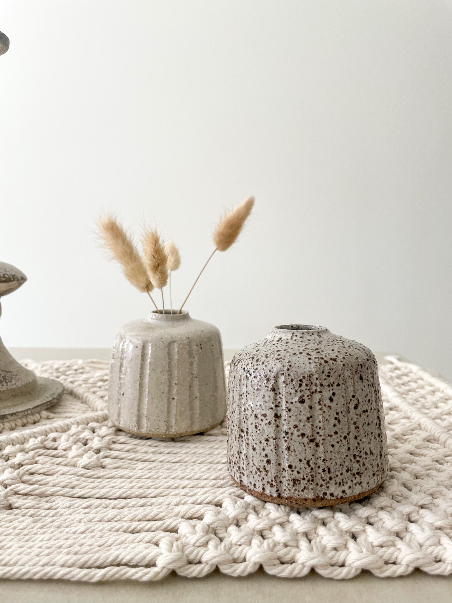 Two small ceramic vases displayed on a macrame table runner and styled with dried flowers