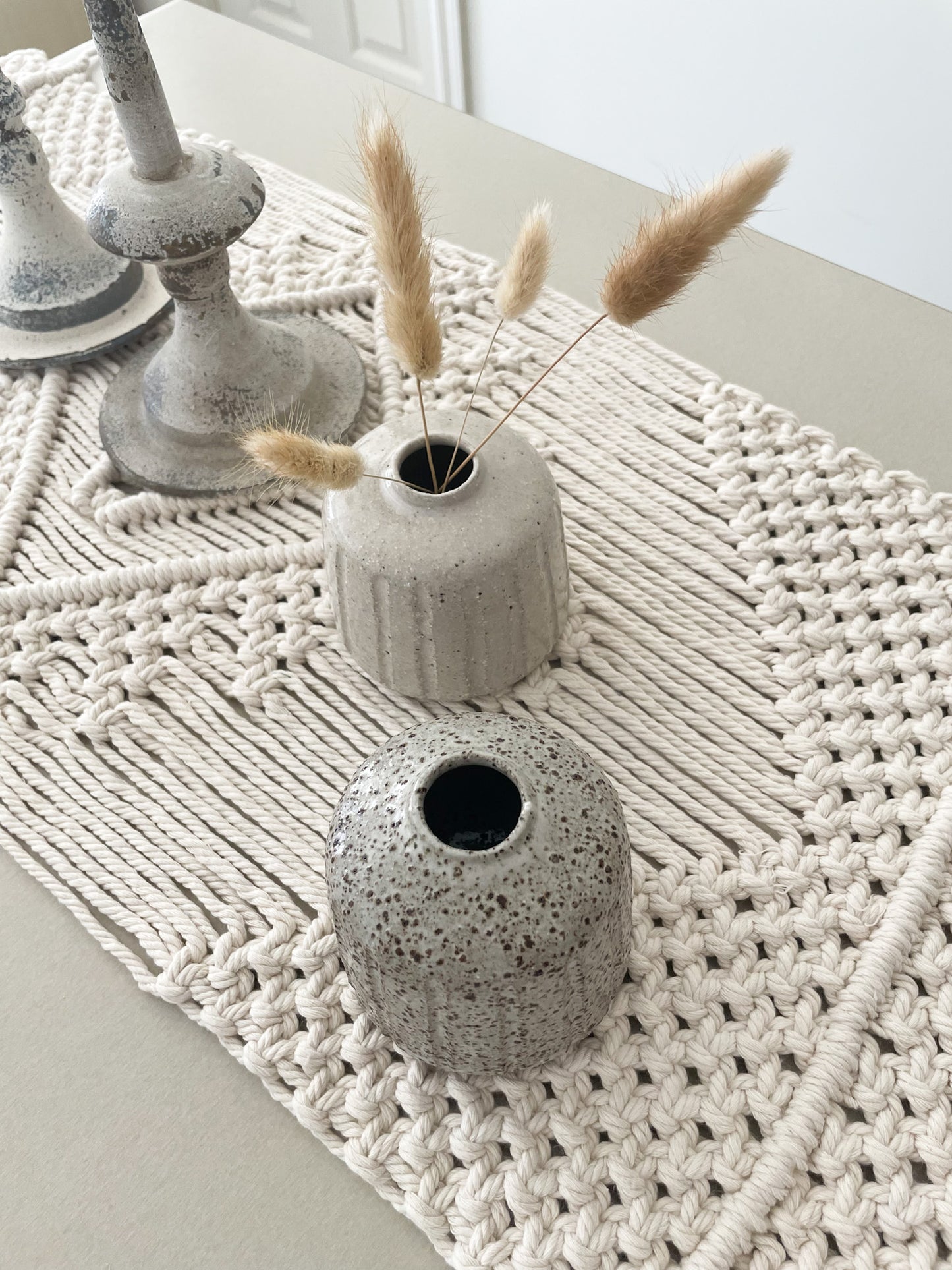 Two small ceramic vases displayed on a table runner and styled with dried flowers
